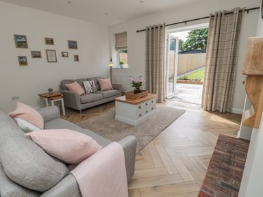 A living room with two sofas and a coffee table near open doors leading to a garden at The Miners Cottage in Scremerston near Berwick-Upon-Tweed
