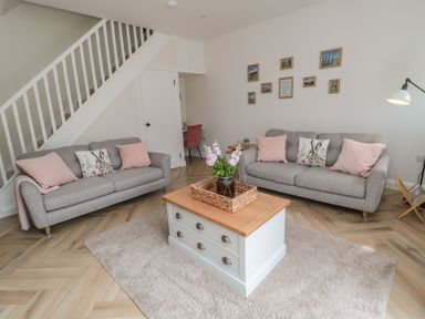 A living room with two grey sofas with pink and rabbit patterned cushions a wooden coffee table with a wicker tray and flowers on a rug at The Miners Cottage in Scremerston near Berwick-Upon-Tweed