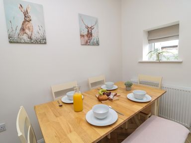 A dining room with a wooden table set for four with bowls plates juice and fruit at The Miners Cottage in Scremerston near Berwick-Upon-Tweed