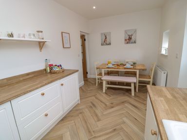 A dining area with a wooden table set for four and a bench with a beige cushion at The Miners Cottage in Scremerston near Berwick-Upon-Tweed