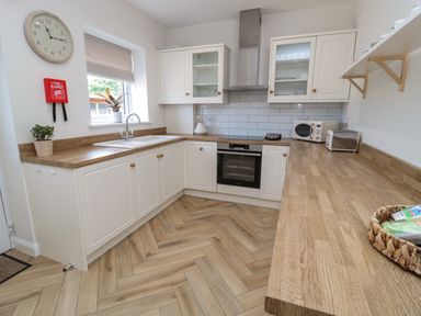 A kitchen with white cabinets wooden countertops a stove microwave toaster and a wall clock at The Miners Cottage in Scremerston near Berwick-Upon-Tweed