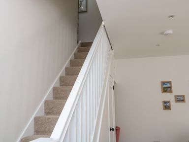 A staircase with beige carpet and white railing next to a white wall with three framed pictures at The Miners Cottage in Scremerston near Berwick-Upon-Tweed