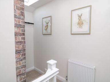 A stairway landing with a white railing a radiator exposed brick wall and two framed animal prints at The Miners Cottage in Scremerston near Berwick-Upon-Tweed