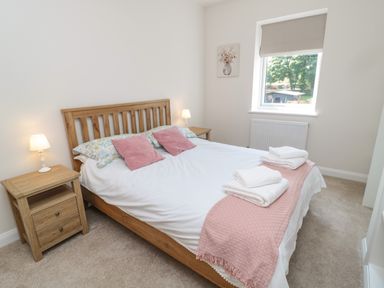 A bedroom with a wooden bed frame pink pillows bedside tables with lamps and a window at The Miners Cottage in Scremerston near Berwick-Upon-Tweed