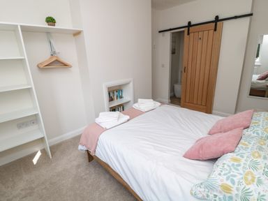 A bedroom with a bed with pink and floral pillows a wooden sliding door and shelves with hangers at The Miners Cottage Scremerston near Berwick-Upon-Tweed