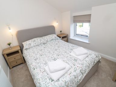 A bedroom with a double bed with floral bedding towels on the bed wooden bedside tables with flowers wall lamps and a window at The Miners Cottage in Scremerston near Berwick-Upon-Tweed