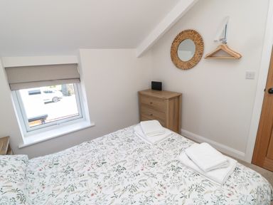 A bedroom with a floral bedspread two sets of folded white towels wooden chest of drawers a round wicker mirror and a window at The Miners Cottage Scremerston near Berwick-Upon-Tweed
