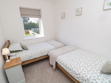 A bedroom with two single beds a bedside table with a lamp a window and framed plant pictures on the wall at The Miners Cottage in Scremerston near Berwick-Upon-Tweed