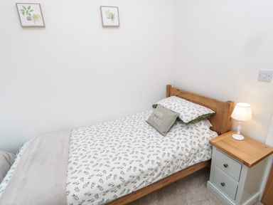 A small bedroom with a single bed with patterned bedding a wooden headboard a bedside table with a lamp and two framed plant pictures on the wall at The Miners Cottage in Scremerston near Berwick-Upon-Tweed