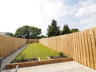 A backyard with a lawn and flower beds along wooden fences at The Miners Cottage in Scremerston near Berwick-Upon-Tweed