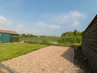A garden with a pebbled area and grass next to a wooden shed and green field at The Miners Cottage in Scremerston near Berwick-Upon-Tweed