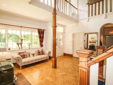An entryway with a beige sofa under a window a wooden staircase and a large mirror at Deer Leap House in Moreton