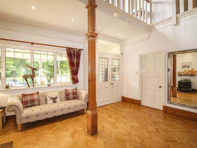 An entrance hall with a beige sofa near windows and a wooden column with double doors and a large mirror at Deer Leap House in Moreton