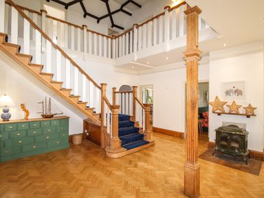 A hallway with a wooden staircase with blue carpet and a green dresser with decorations at Deer Leap House in Moreton