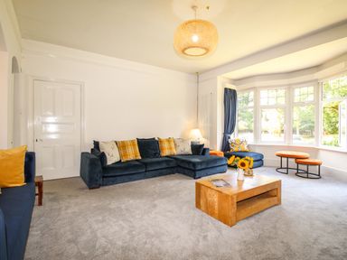 A living room with blue sofas yellow cushions a wooden coffee table and large windows at Deer Leap House in Moreton