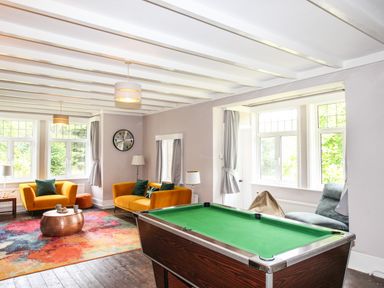 A living room with a pool table two yellow sofas colorful rug and large windows at Deer Leap House in Moreton