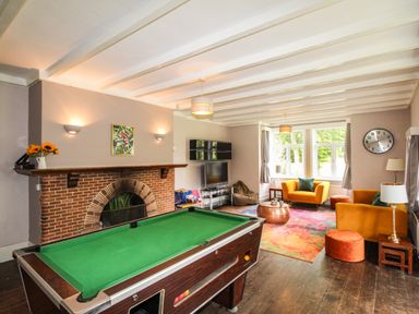 A room with a pool table a brick fireplace seating area with chairs and a sofa and a television at Deer Leap House in Moreton