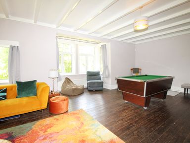 A room with a pool table armchairs a yellow sofa with pillows a floor lamp and curtains at Deer Leap House in Moreton