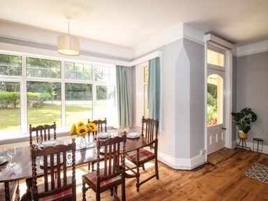 A dining room with a wooden table and chairs set for a meal with sunflowers on the table at Deer Leap House in Moreton