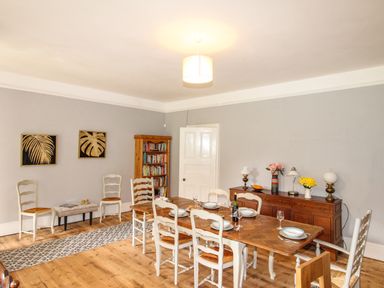 A dining room with a wooden dining table and chairs a wooden cabinet with lamps and flowers and a bookshelf with books at Deer Leap House in Moreton