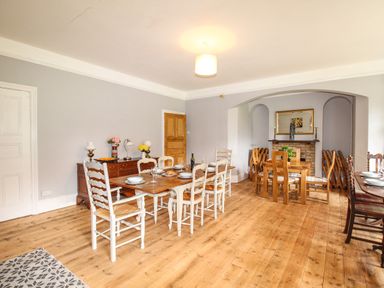 A dining room with two wooden dining tables and chairs a sideboard with lamps and flowers and a fireplace at Deer Leap House in Moreton