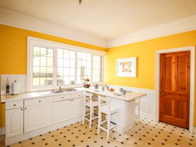 A kitchen with white cabinets a wooden door and a window above the sink at Deer Leap House in Moreton