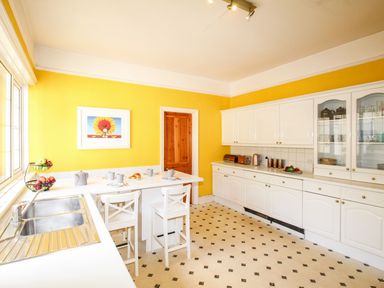 A kitchen with yellow walls white cabinets and a breakfast bar with chairs at Deer Leap House in Moreton