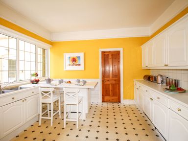 A kitchen with white cabinets yellow walls a wooden door and a breakfast table with two chairs at Deer Leap House in Moreton
