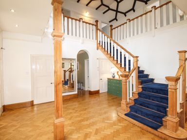 An entry hall with wooden staircase covered in blue carpet and green chest of drawers at Deer Leap House in Moreton
