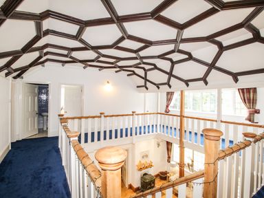 An upper floor landing with blue carpet and wooden railing overlooking a living room at Deer Leap House in Moreton