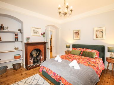 A bedroom with a green bed and orange patterned bedding next to a brick fireplace and wooden shelves at Deer Leap House in Moreton