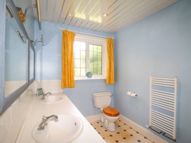 A bathroom with double sinks a toilet with a wooden seat yellow curtains and a white towel radiator at Deer Leap House in Moreton