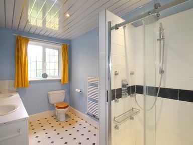 A bathroom with a shower enclosure toilet with wooden seat double sink and yellow curtains at Deer Leap House in Moreton