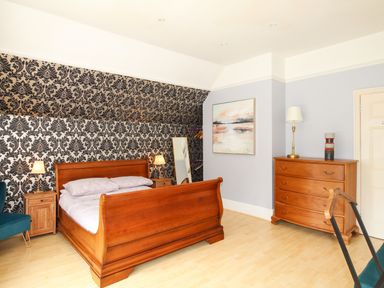 A bedroom with a wooden bed chest of drawers and patterned wallpaper at Deer Leap House in Moreton