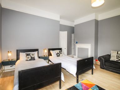 A bedroom with two single beds, bedside tables with lamps, a black armchair, and a colorful rug at Deer Leap House in Moreton