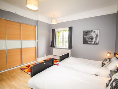 A bedroom with two single beds a window wardrobes and a lion picture on the wall at Deer Leap House in Moreton