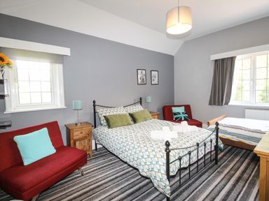 A bedroom with a double bed and a single bed two red armchairs and a striped carpet at Deer Leap House in Moreton
