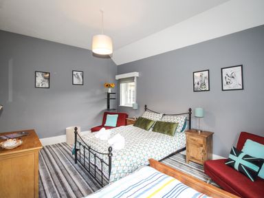 A bedroom with two beds a wooden dresser two red chairs and framed animal pictures on gray walls at Deer Leap House in Moreton
