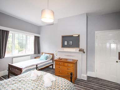 A bedroom with two single beds a wooden dresser and a window with curtains at Deer Leap House in Moreton