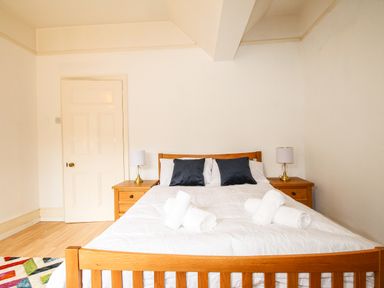 A bedroom with a wooden double bed with white bedding and two black pillows beside wooden nightstands with lamps at Deer Leap House in Moreton