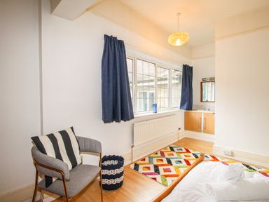 A bedroom with a chair and a pillow near a window with blue curtains at Deer Leap House in Moreton