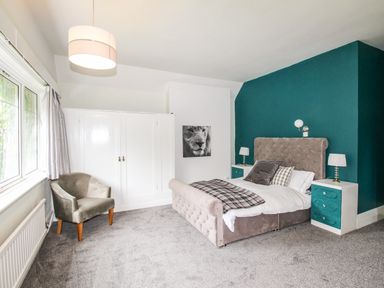 A bedroom with a bed two bedside tables a chair a large window and a wardrobe at Deer Leap House in Moreton
