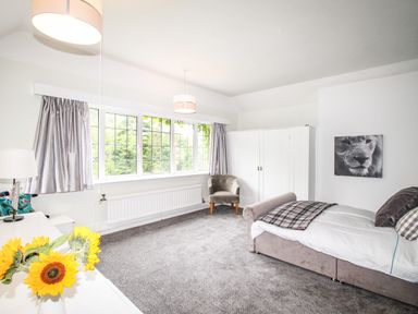 A bedroom with a bed a chair a wardrobe a window with curtains and a vase with sunflowers at Deer Leap House in Moreton