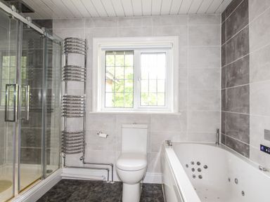 A bathroom with a glass shower enclosure a toilet a window a towel warmer radiatior and a bathtub with jets at Deer Leap House in Moreton