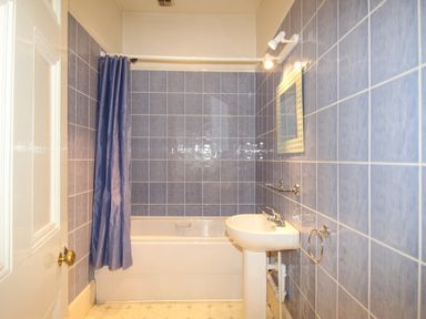 A bathroom with a bathtub shower with blue tiles and a curtain a sink with a mirror above it and a towel ring on the wall at Deer Leap House in Moreton