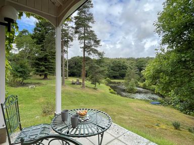A patio with metal chairs and table overlooking a grassy yard with trees and a pond at Deer Leap House in Moreton