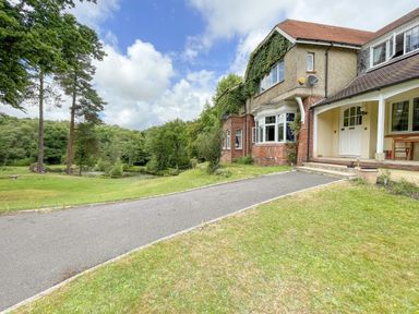 An exterior view of a two-story house with a driveway and surrounding lawn and trees at Deer Leap House in Moreton