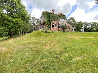 A brick and stone house covered with ivy on a grassy hill surrounded by trees at Deer Leap House in Moreton