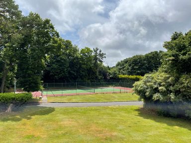 An outdoor tennis court surrounded by trees and greenery at Deer Leap House in Moreton