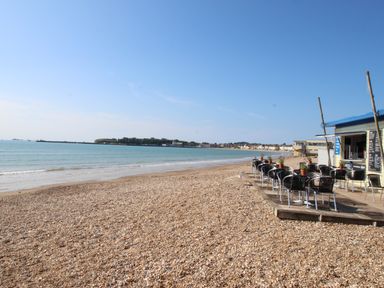 A pebble beach with outdoor tables and chairs next to a small building by the sea at Deer Leap House in Moreton